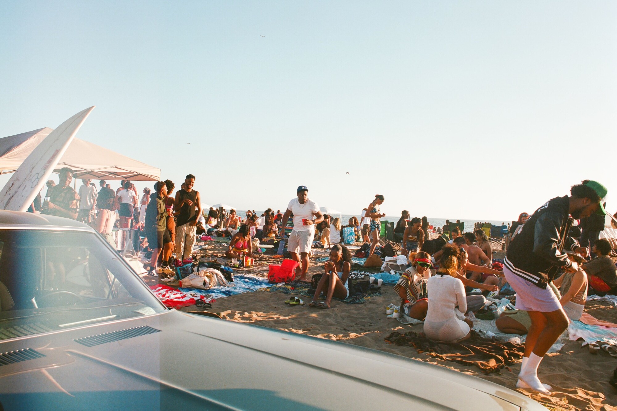 Photo of a crowded beach taken from next to the hood of a car 