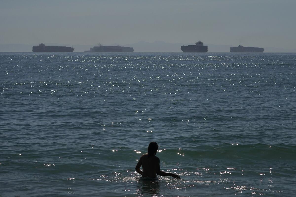 Man wading in ocean with container ships in the distance