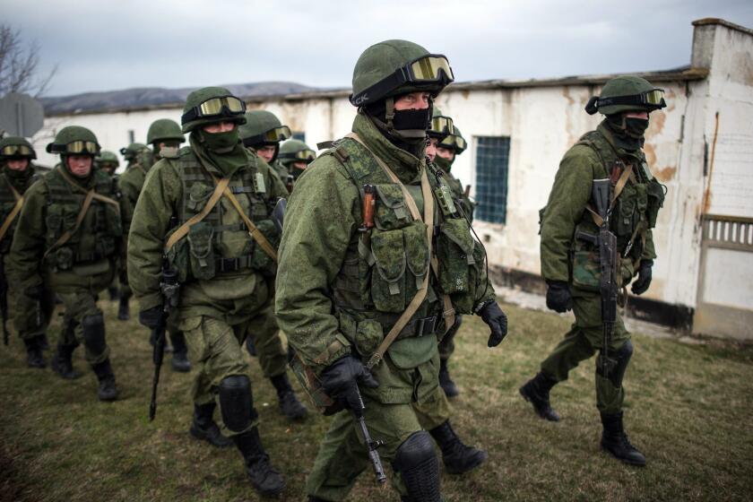 Armed men in military uniform walk outside the territory of a Ukrainian military unit in the village of Perevalnoye, outside Simferopol, Ukraine.