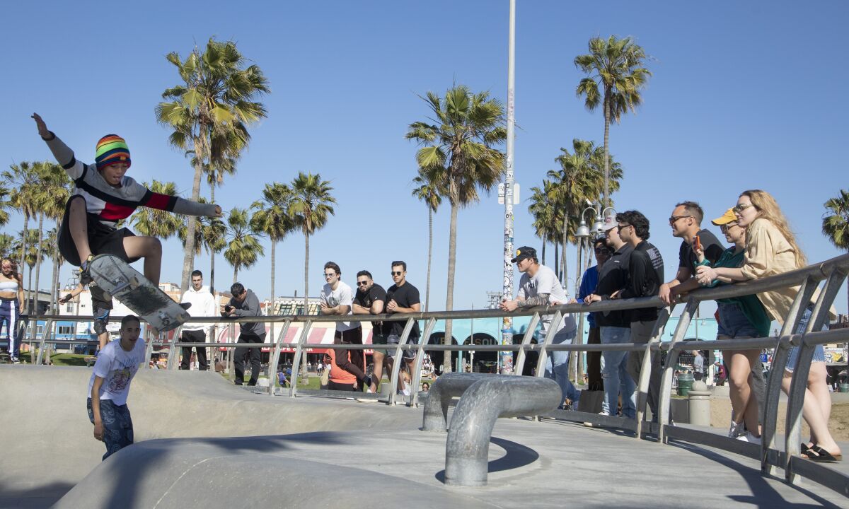 A skateboarder does a trick as people watch at the Venice Beach skatepark