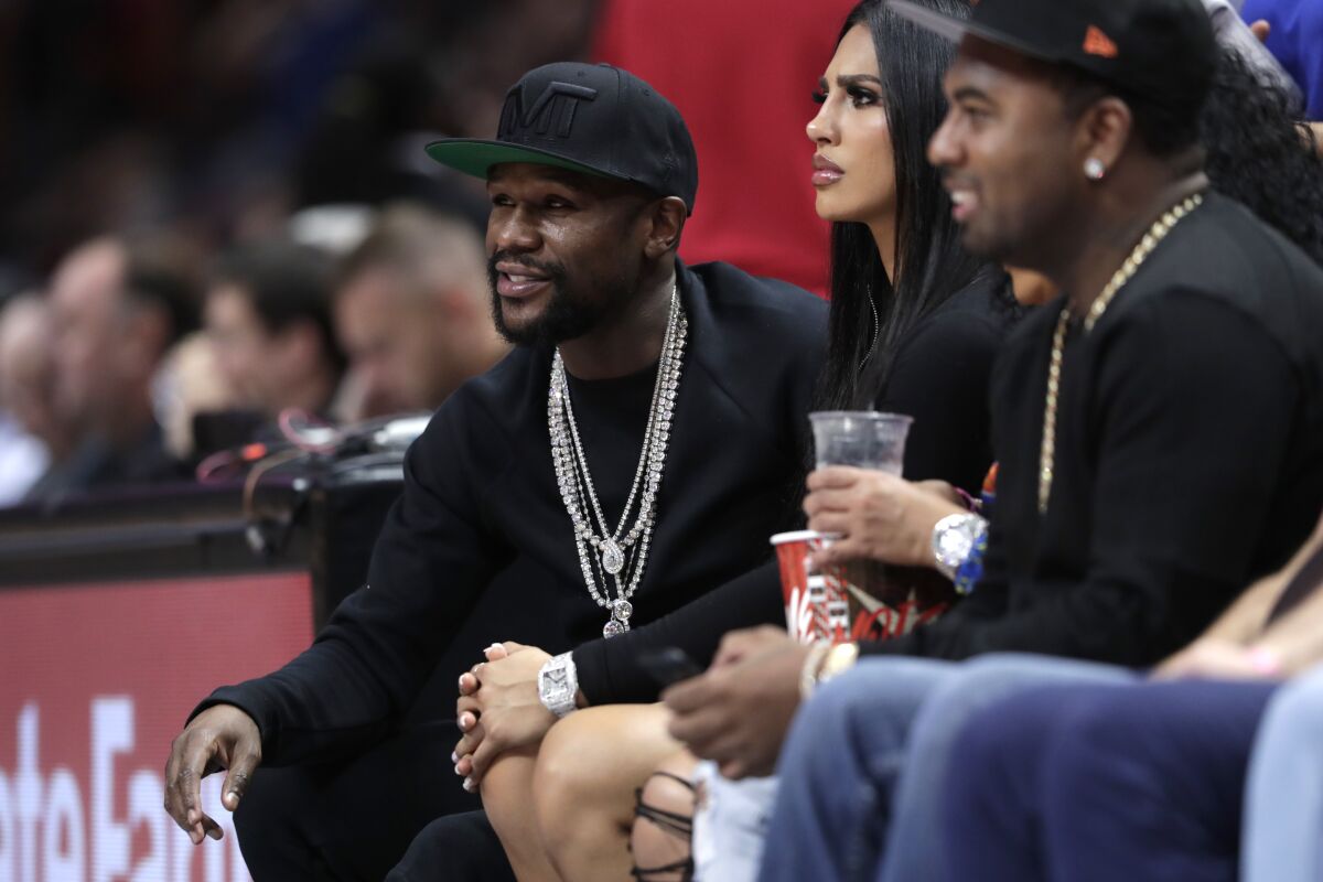 Floyd Mayweather, left, watches an NBA basketball game in Miami.
