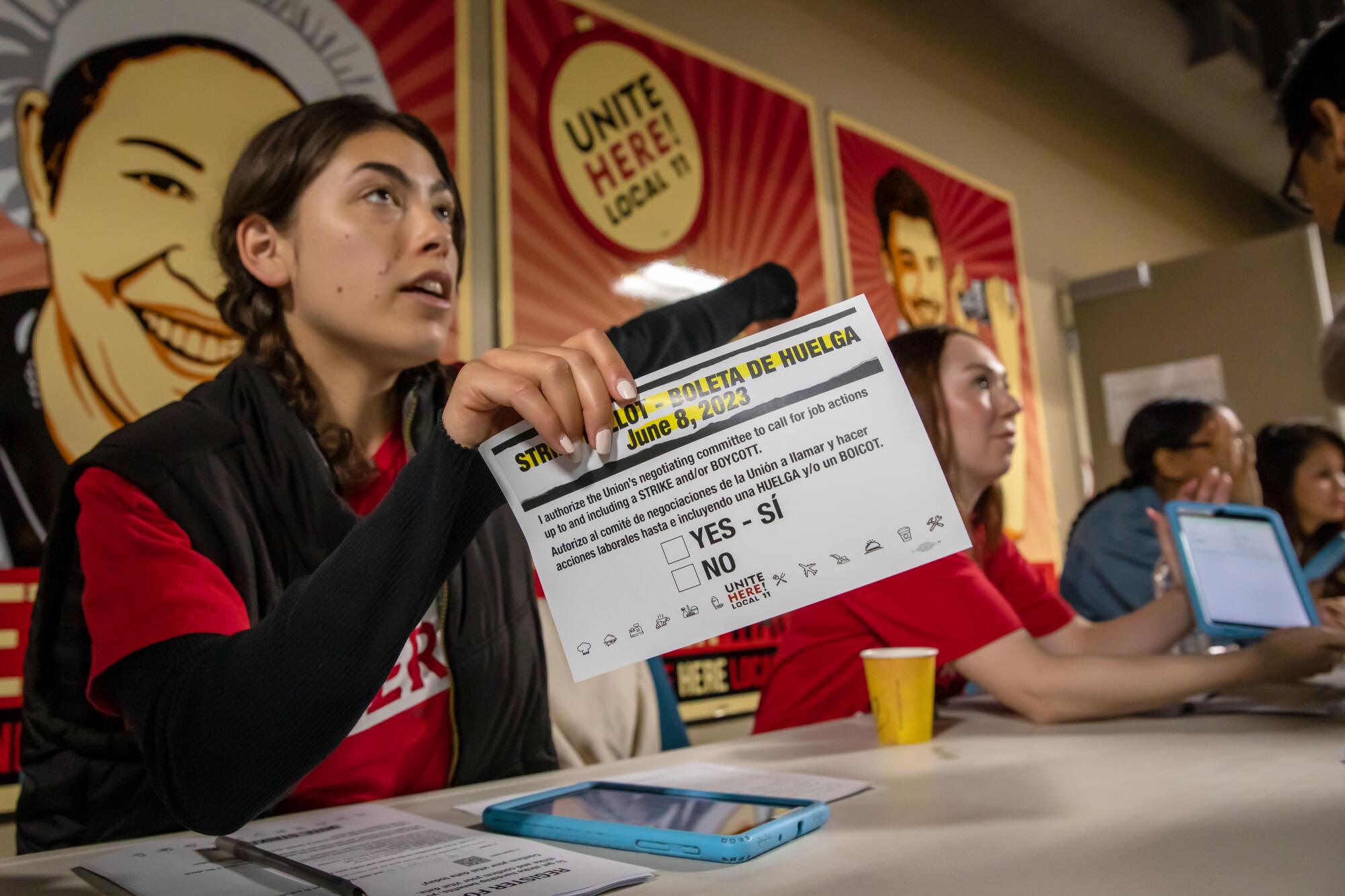 A woman holds a strike authorization ballot with union posters behind her.