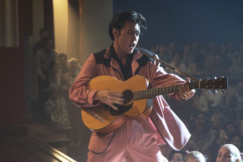 Austin Butler wearing a pink suit and holding a guitar on stage