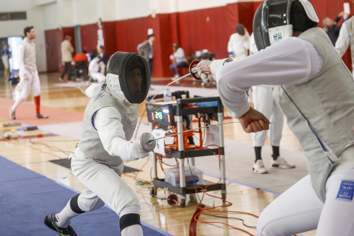 Two fencers spar in a gymnasium.