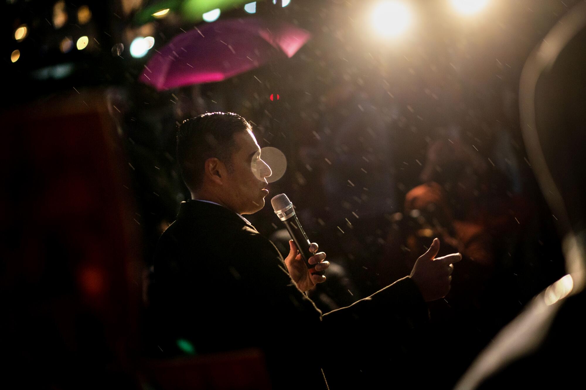 Robert Garcia talks into a microphone outside at night as rain falls