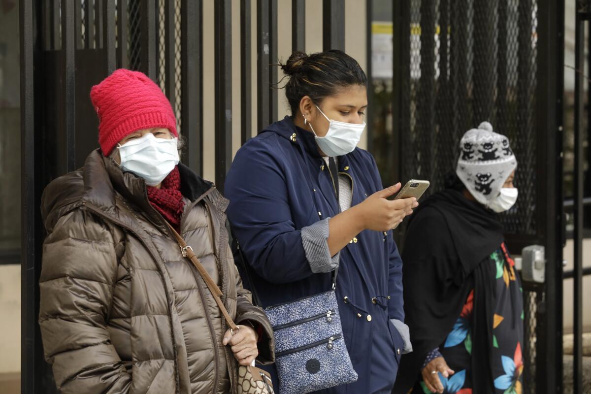 People wearing masks wait for a Lyft in downtown Los Angeles on Tuesday.