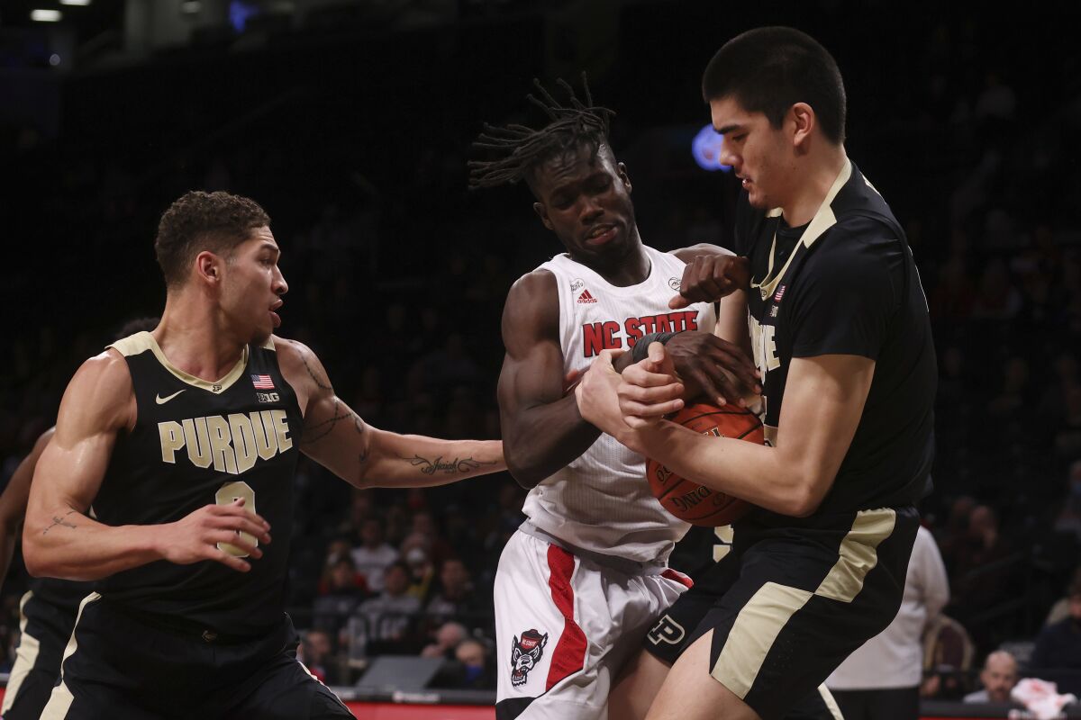North Carolina State's Ebenezer Dowuona, center, of Ghana, fights for possession with Purdue's Mason Gillis, left, and Zach Edey during the first half of an NCAA college basketball game Sunday, Dec. 12, 2021, in New York. (AP Photo/Jason DeCrow)