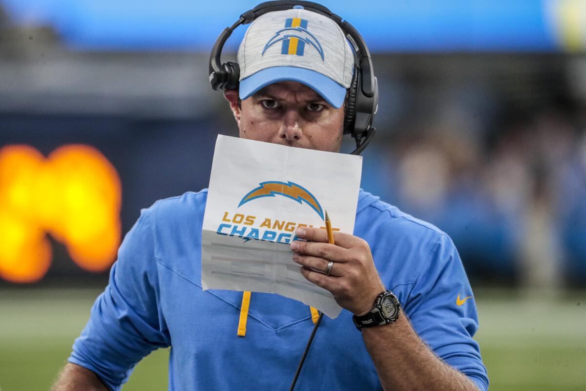 Chargers coach Brandon Staley paces the sideline while holding up a piece of paper.