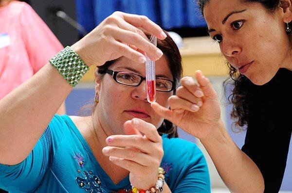 Lorena Marin, right, helps Beatriz Garcia during the measurement portion of the Lennox School District's "Learn How to Care for Your Child's Health" program at Moffett Elementary School. Using red juice, participants are shown how to measure the correct amount of medicine for their children. See full story