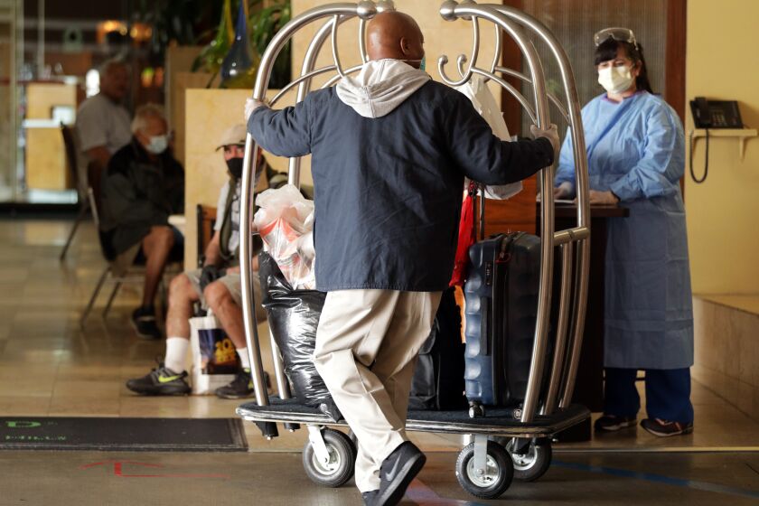 LOS ANGELES, CA - APRIL 06: Omar Spry of Los Angeles Housing Community Investment Department, pushes a cart of residents' bags into a West L.A. hotel that has been turned into housing for the homeless during the coronavirus pandemic. The homeless housing is through a program with the Hotel Assn. of Los Angeles, Los Angeles County, city of Los Angeles and non-profits. (Myung J. Chun / Los Angeles Times)