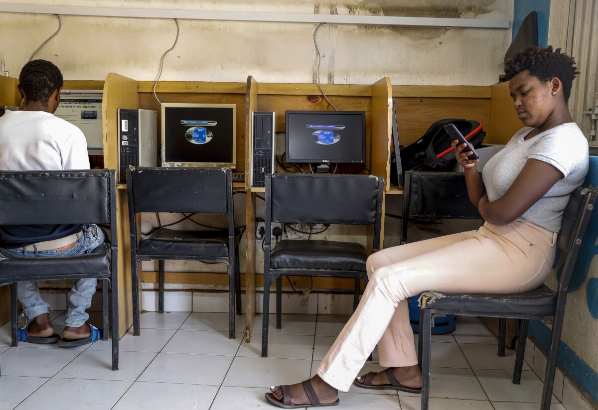 FILE - A customer uses the Wi-Fi on her mobile phone at an internet cafe in the low-income Kibera neighborhood of Nairobi, Kenya on Sept. 29, 2021. Facebook has failed to catch Islamic State group and al-Shabab extremist content in posts aimed at East Africa as the region remains under threat from violent attacks and Kenya prepares to vote in a closely contested national election, according to a new study released Wednesday, June 15, 2022. (AP Photo/Brian Inganga, File)