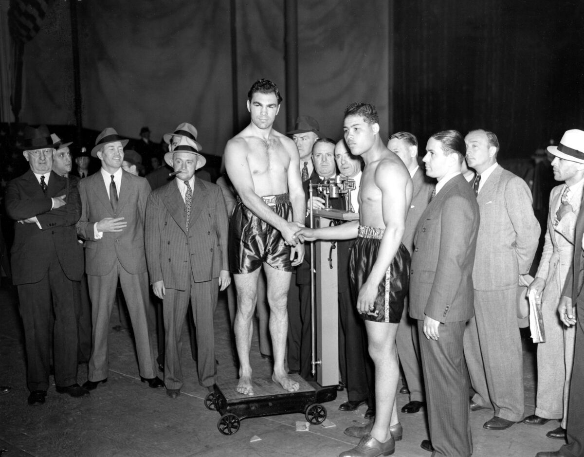 Max Schmeling, on scale, and Joe Louis shake hands at the weigh-in ceremony for their bout at Yankee Stadium on June 18, 1936.
