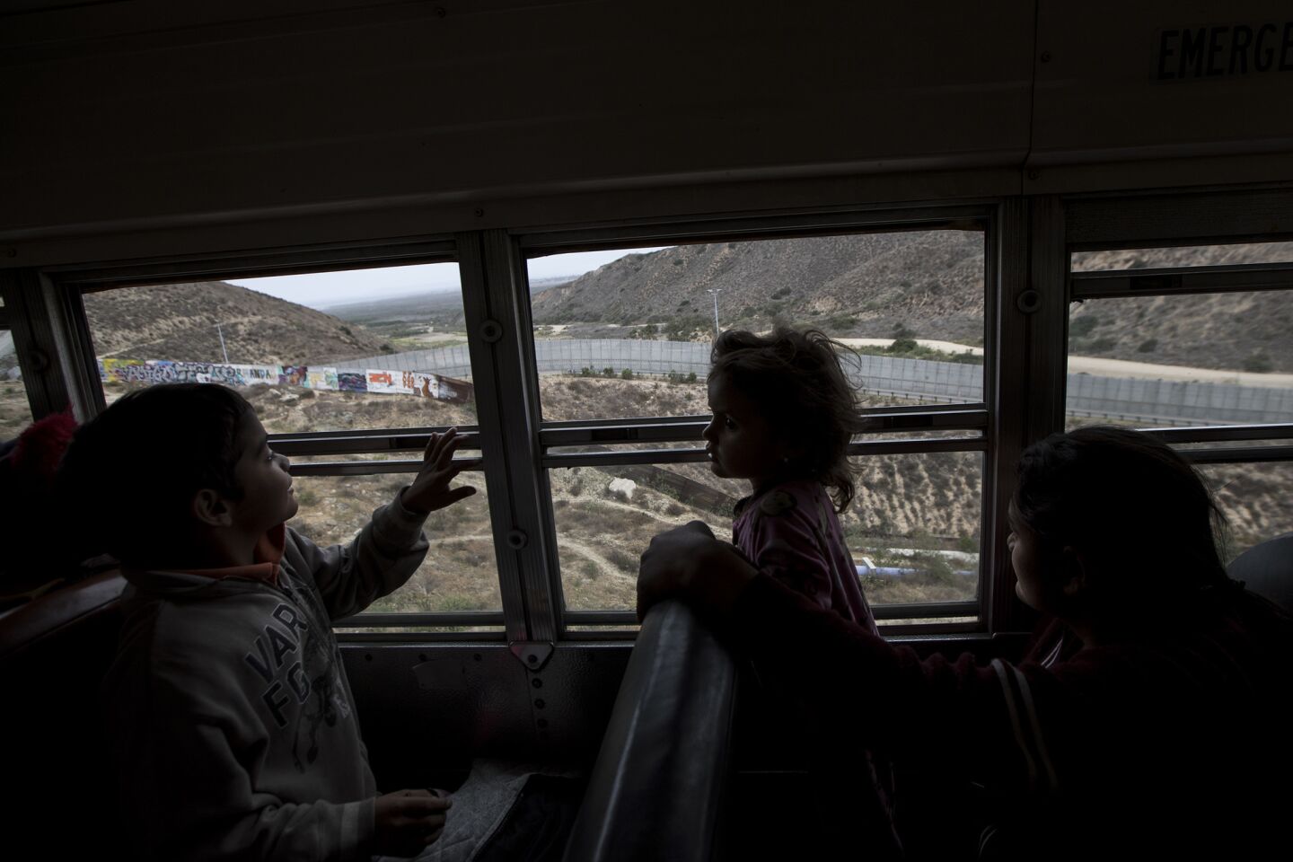 Central American children who have traveled for weeks with a caravan of immigrants, peer out at the border wall from a bus in Tijuana, Mexico.