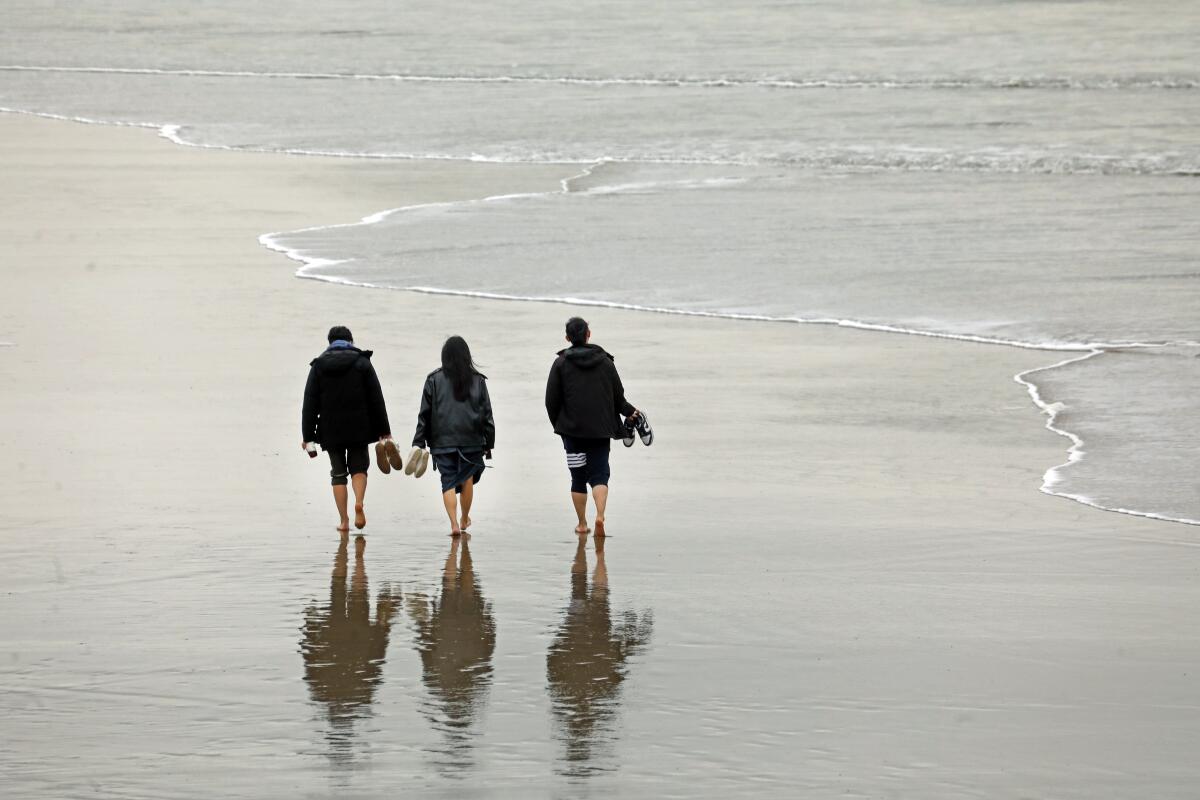 Three people walk barefoot on the beach along the shore in Santa Monica.