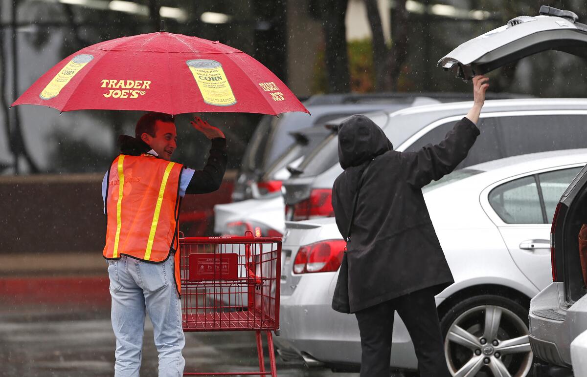 A Trader Joe's employee helps a shopper unload groceries while giving her cover with an umbrella.