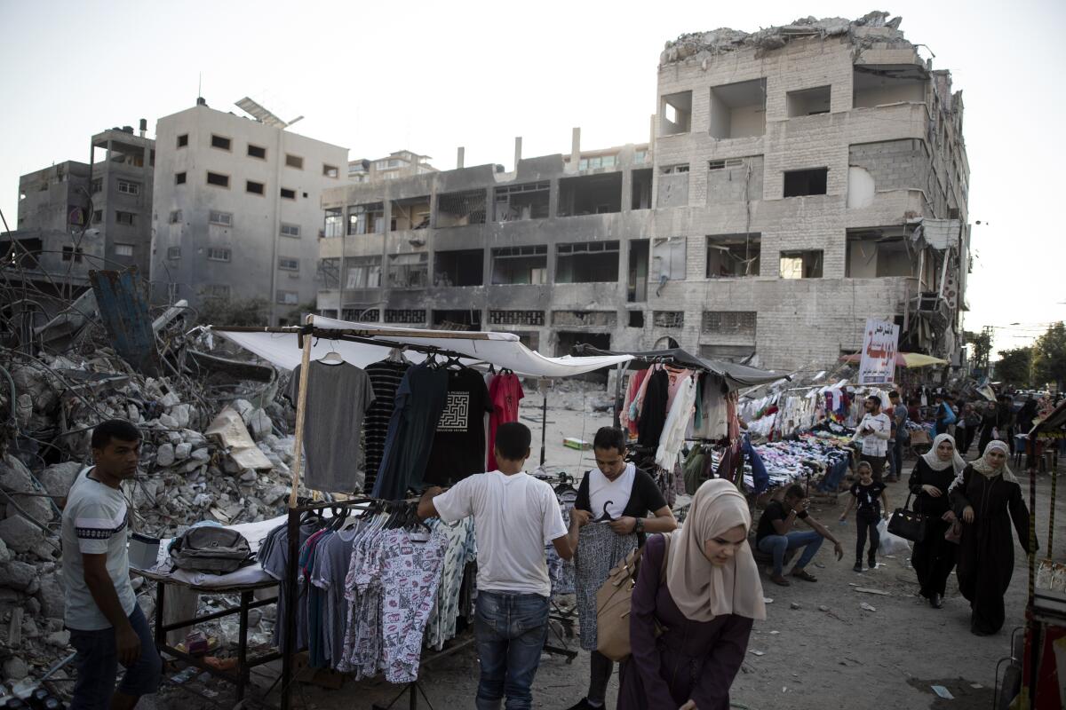 FILE - In this Sunday, July 18, 2021, file photo, Palestinian street vendors display clothes for sale next to the rubble of destroyed buildings were hit by Israeli airstrikes during an 11-day war between Gaza's Hamas rulers and Israel, in Gaza City. Israel allowed dozens of truckloads of construction materials into the Gaza Strip on Tuesday, Aug. 31, easing a tight blockade it has maintained on the Hamas-ruled territory since last May. (AP Photo/Khalil Hamra, File)
