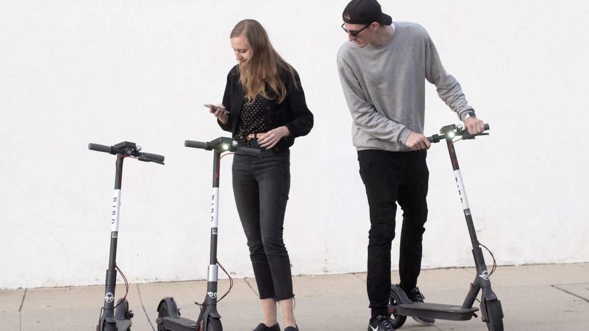 Kylee Kramer, left, and Adam Baker, right, both of Altadena, use an app to pay and unlock Bird Scooters near Lake Avenue in Altadena.