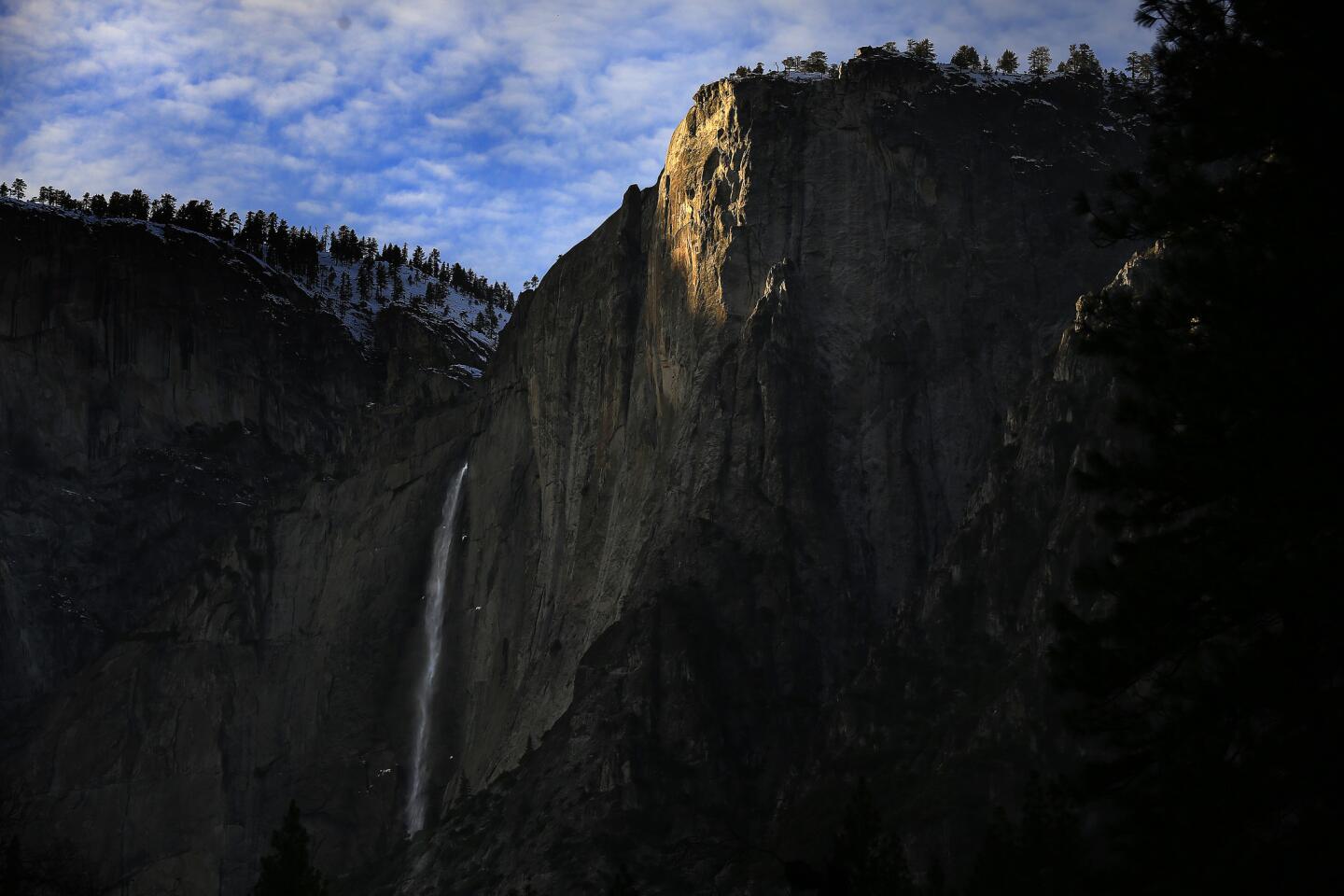 Sunlight sets a granite cliff aglow above Upper Yosemite Falls as recent storms have brought the falls back to life in Yosemite National Park.