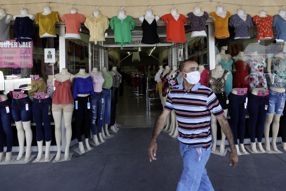 A man in a mask walks past a clothing shop with several mannequins in Calexico, California