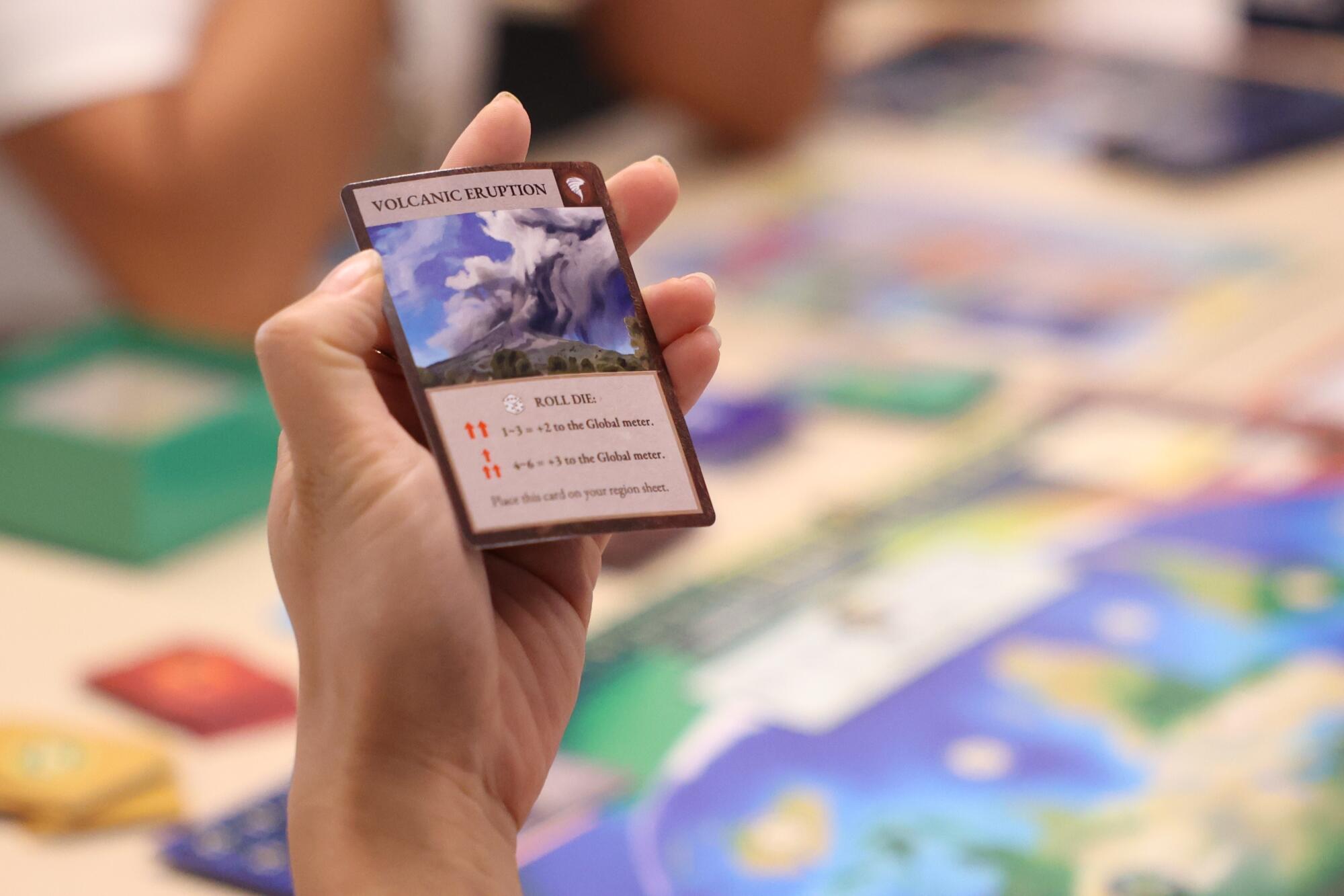 A hand holding a card for a volcanic eruption.