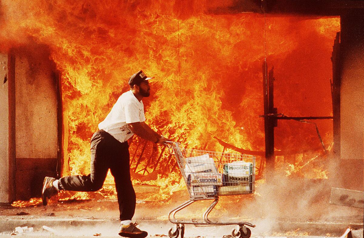 A looter wheels a shopping cart full of diapers past a burning market on April 30, 2992.