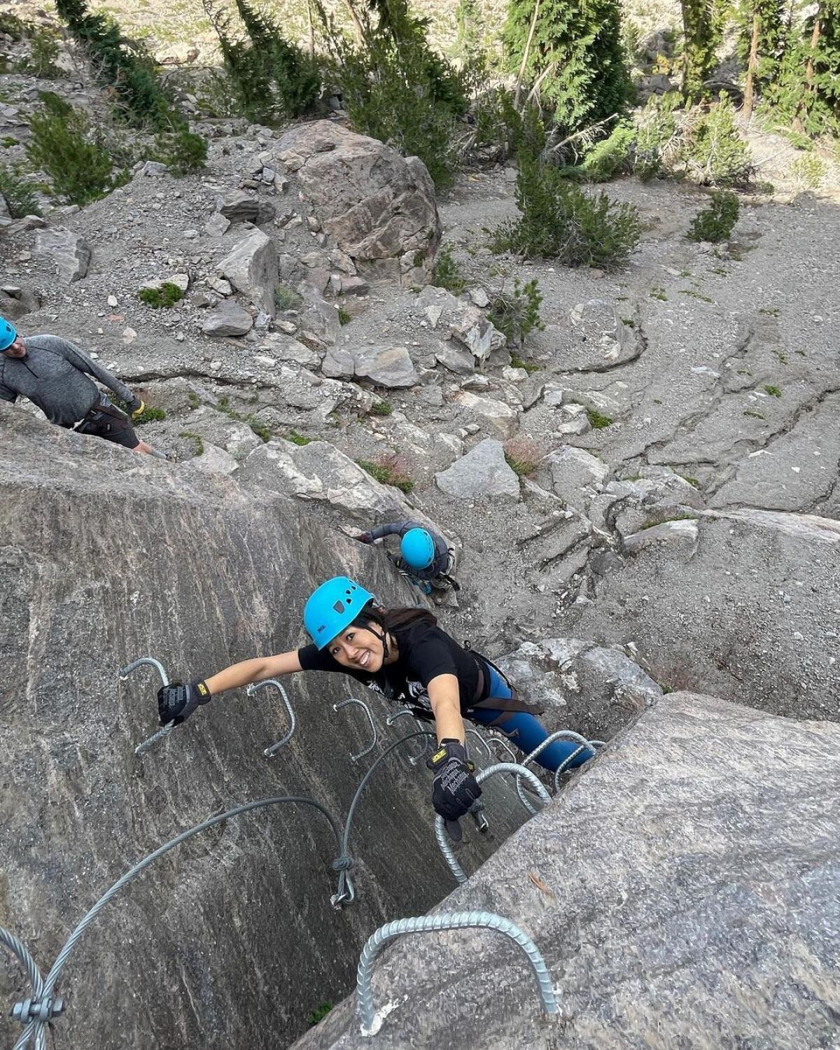 A woman smiles up at the camera as she climbs rocks in the mountains of Mammoth Lakes 