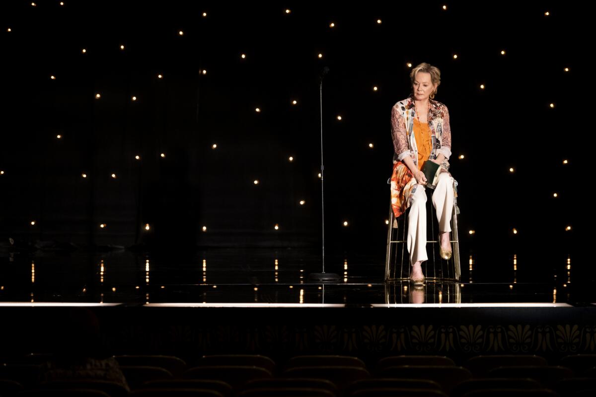 A woman sitting on a stool onstage.