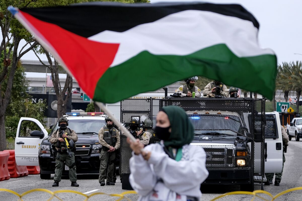 A demonstrator waves the flag of Palestine as police officers guard outside the Federal Building during a protest against Israel and in support of Palestinians, Saturday, May 15, 2021, in the Westwood section of Los Angeles. (AP Photo/Ringo H.W. Chiu)
