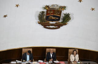 Three people seated below a crest