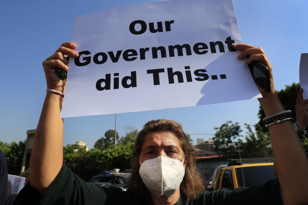 A person in a mask holds up a sign that says "Our government did this."