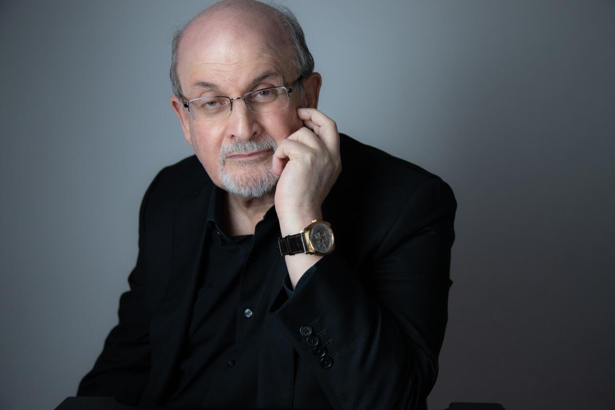 A balding man with glasses in a dark shirt, his hand resting on his cheek