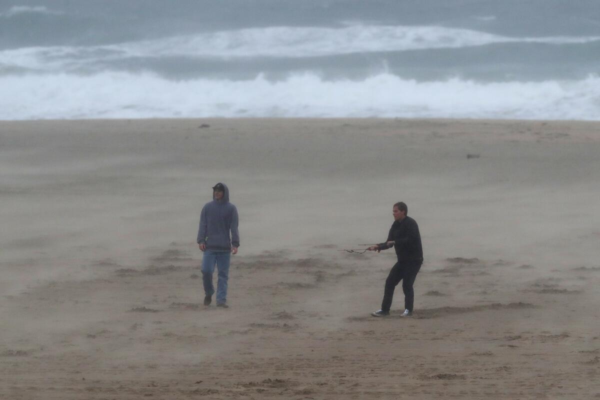 Two men brave the wind and rain as they play with a surfing kite on the south side of the Huntington Beach Pier.
