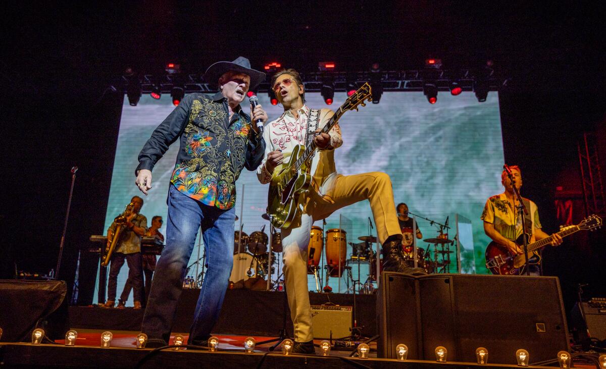 The Beach Boys' Mike Love, left,  sings, and John Stamos plays guitar on a stage