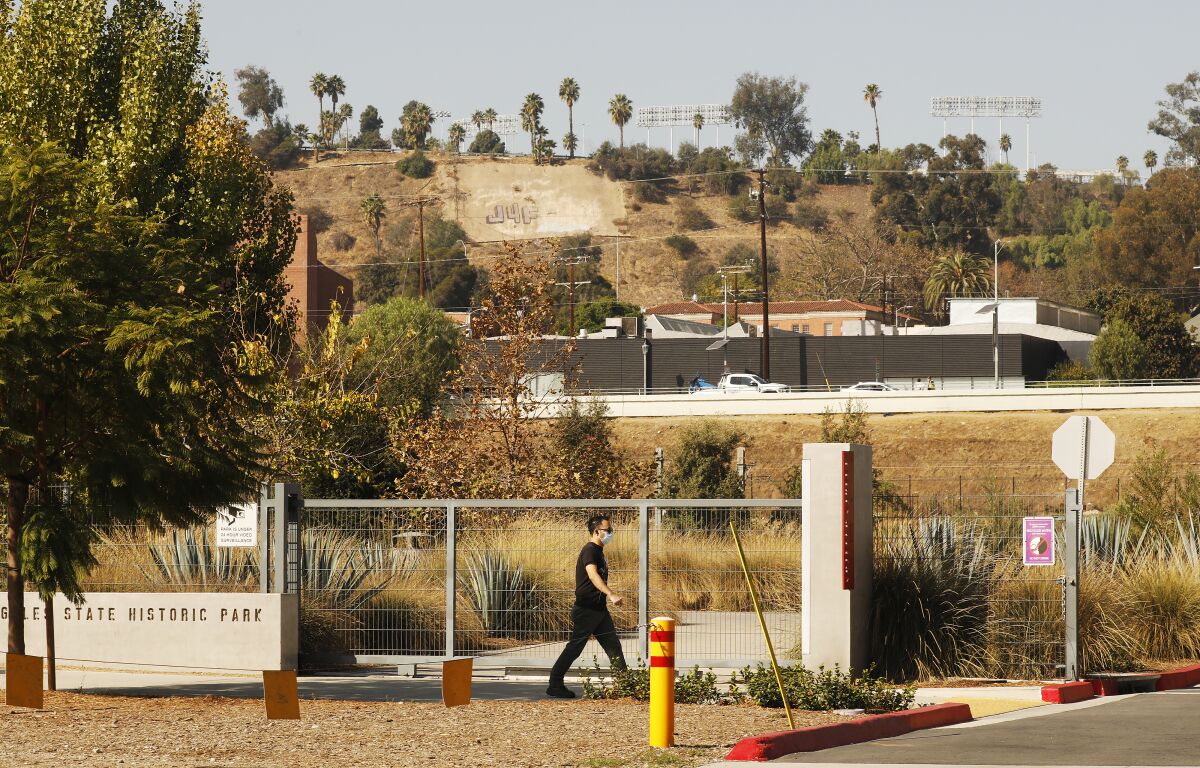 A man in a mask walks on the sidewalk in front of the gate to Los Angeles State Historic Park