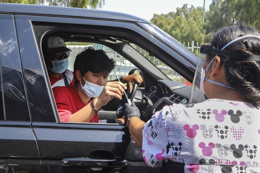 CHULA VISTA, CA - AUGUST 28: Jorge Angel Llamas (left) does a self swab Covid-19 test under the supervision of RN Karen Barringer (right) at the San Diego County Aquatica Testing Site on Friday, Aug. 28, 2020 in Chula Vista, CA. (Eduardo Contreras / The San Diego Union-Tribune)