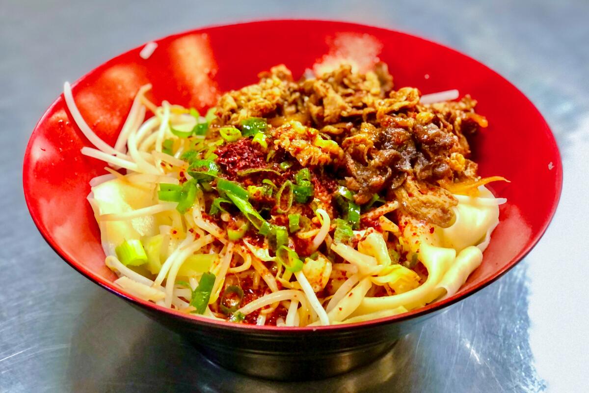A red bowl with noodles topped with scallions, bean sprouts and a red sauce