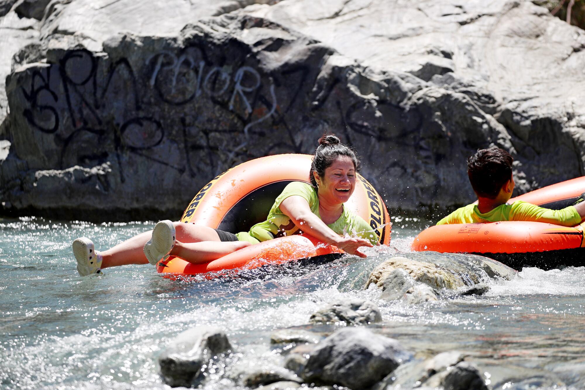 Two people float and play in bright orange innertubes in a river.