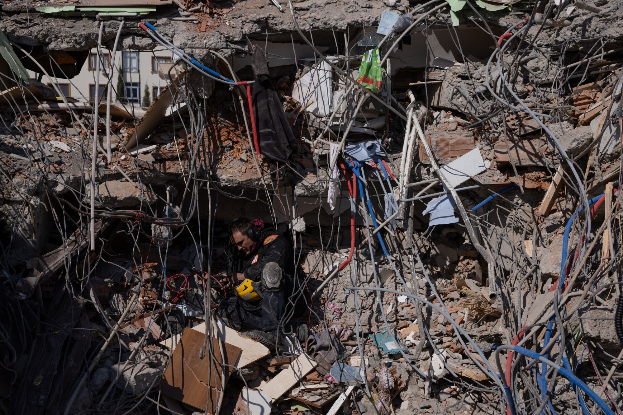 A search and rescue team member stands amid rubble and twisted metal tubes.