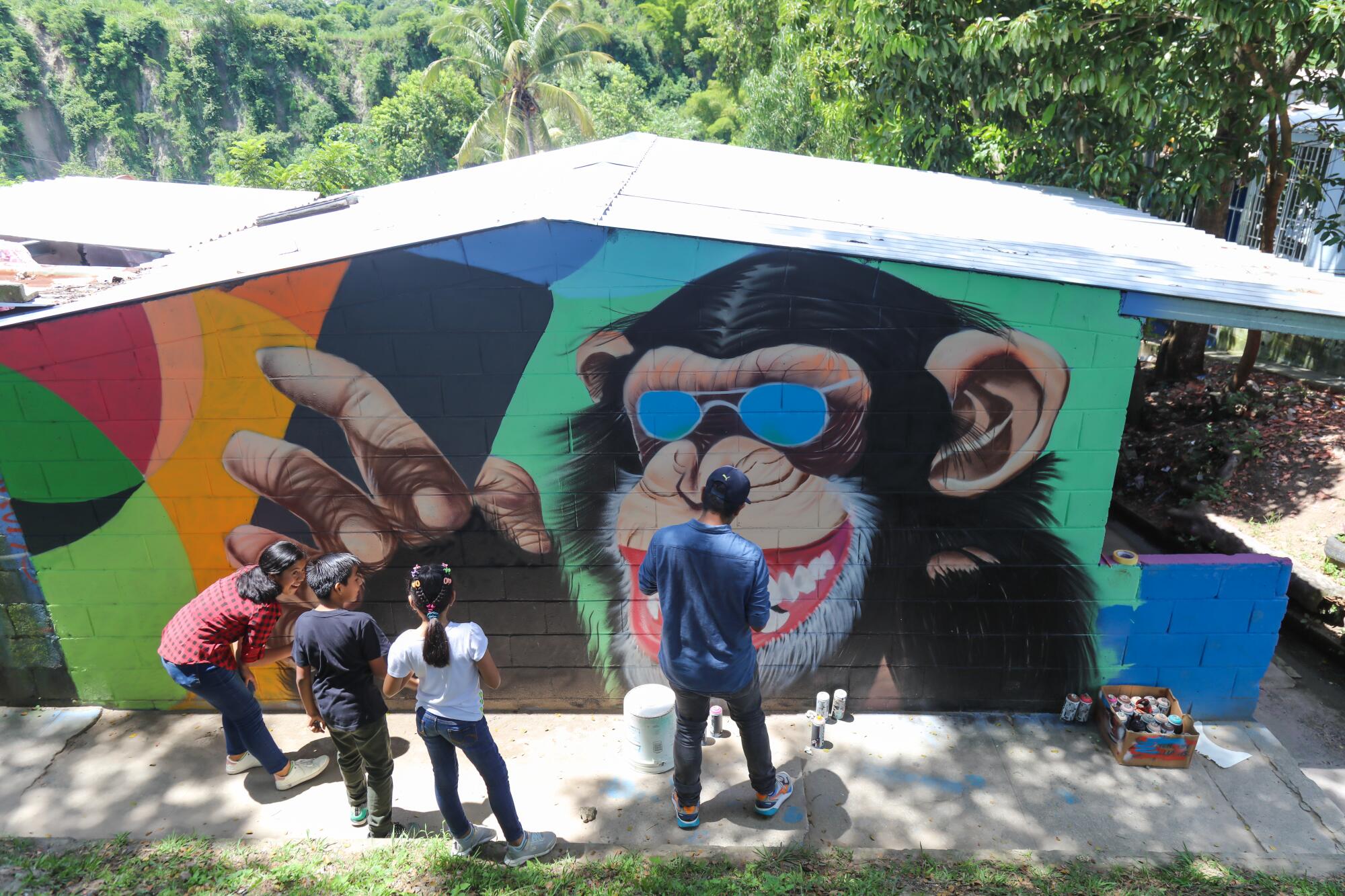 People stand in front of a mural of a monkey wearing sunglasses