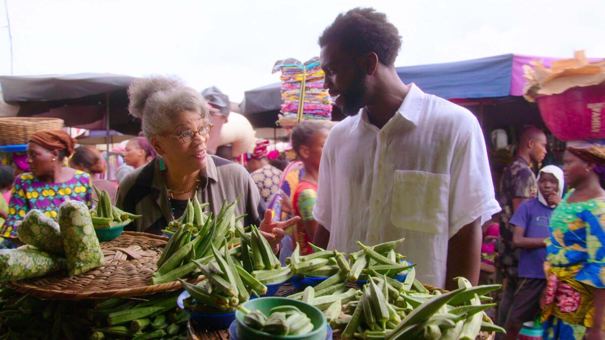 A woman and a man talk to each other at an open-air market. 