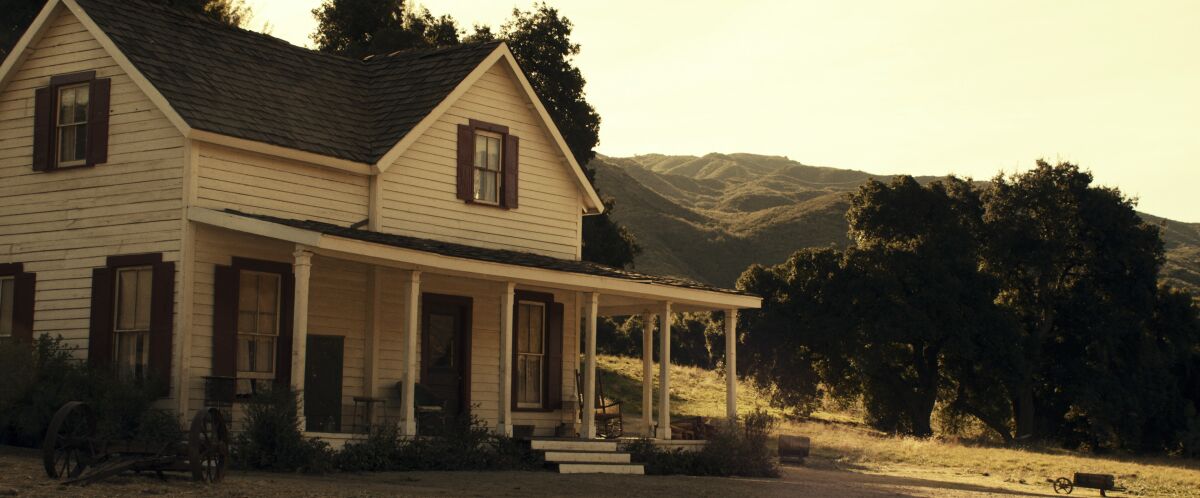 A deceptively bucolic setting, a white clapboard house with mountains in the background.