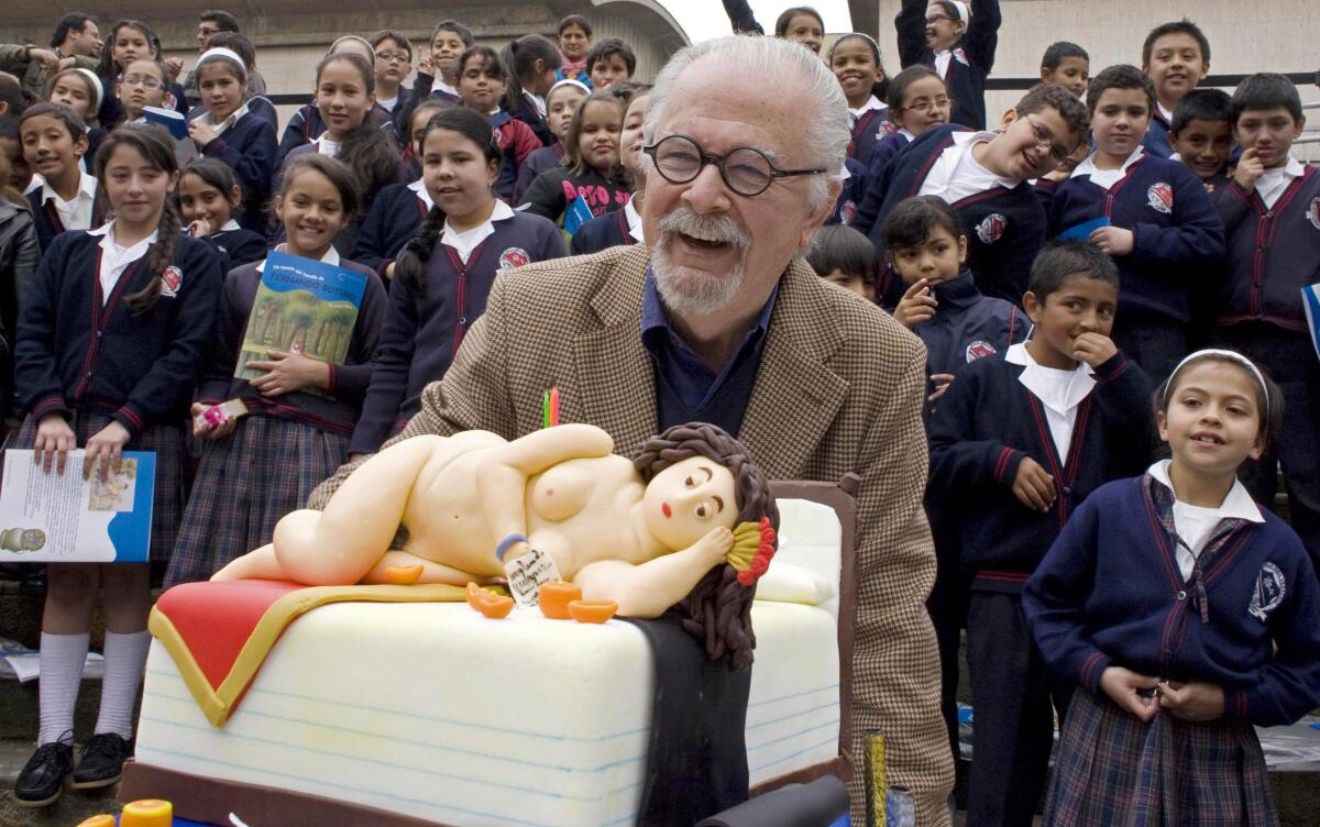 Fernando Botero, a man with white hair and glasses, poses behind a cake decorated with a plump reclining woman