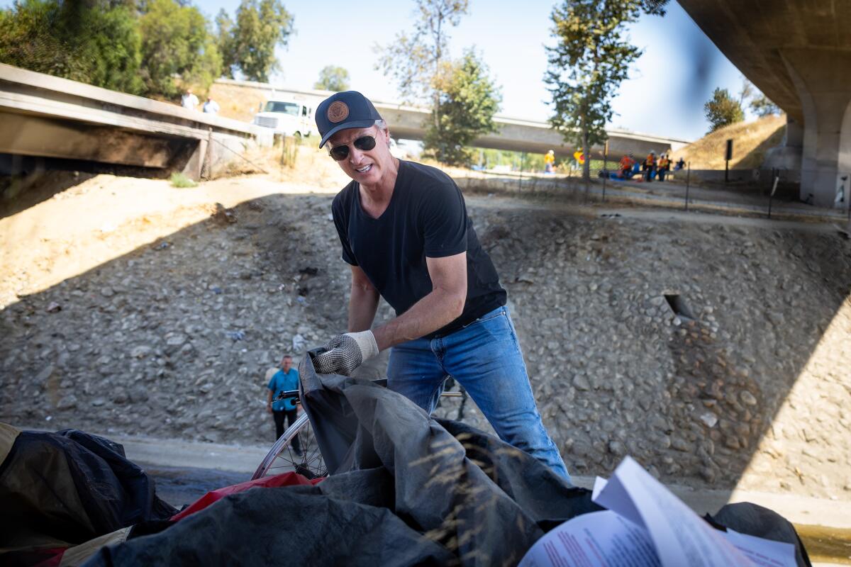 A man adds an item to a trash bag in a channel under two bridges.