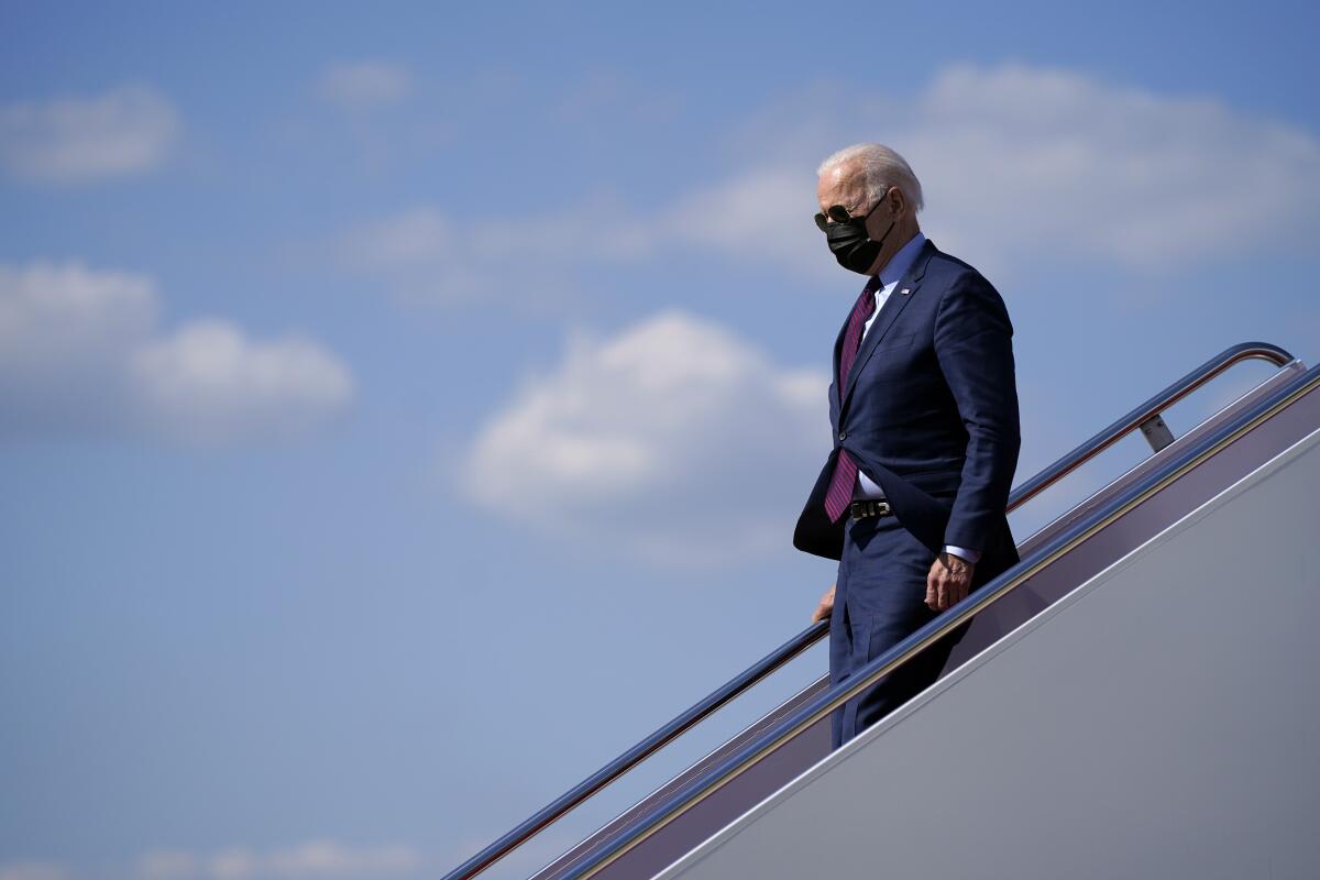 President Biden, in sunglasses and mask, walks down airplane steps.
