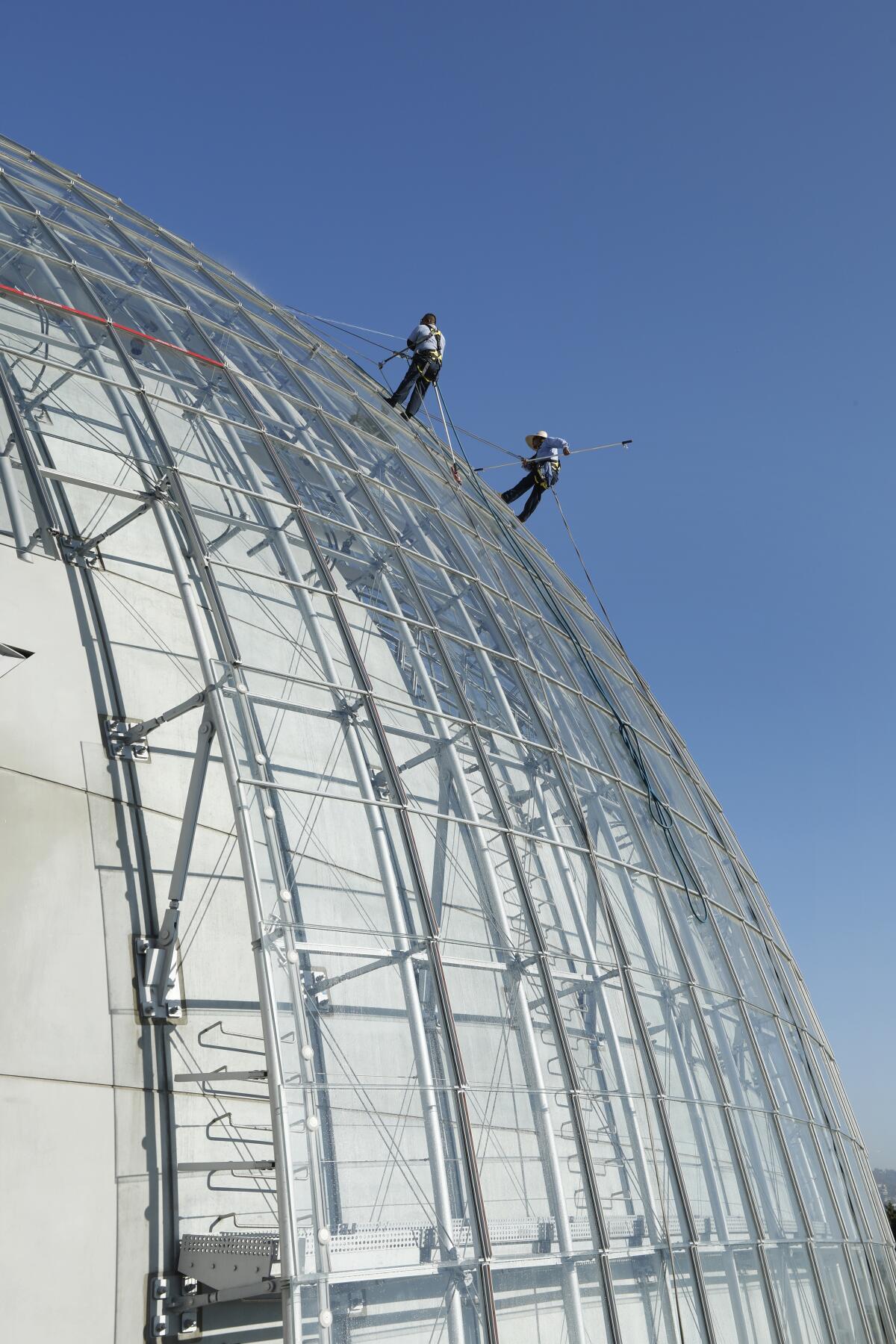 Window washers Mario Guzman, left, and Jesus Garcia clean windows of the Academy Museum of Motion Pictures Aug. 27, 2021 