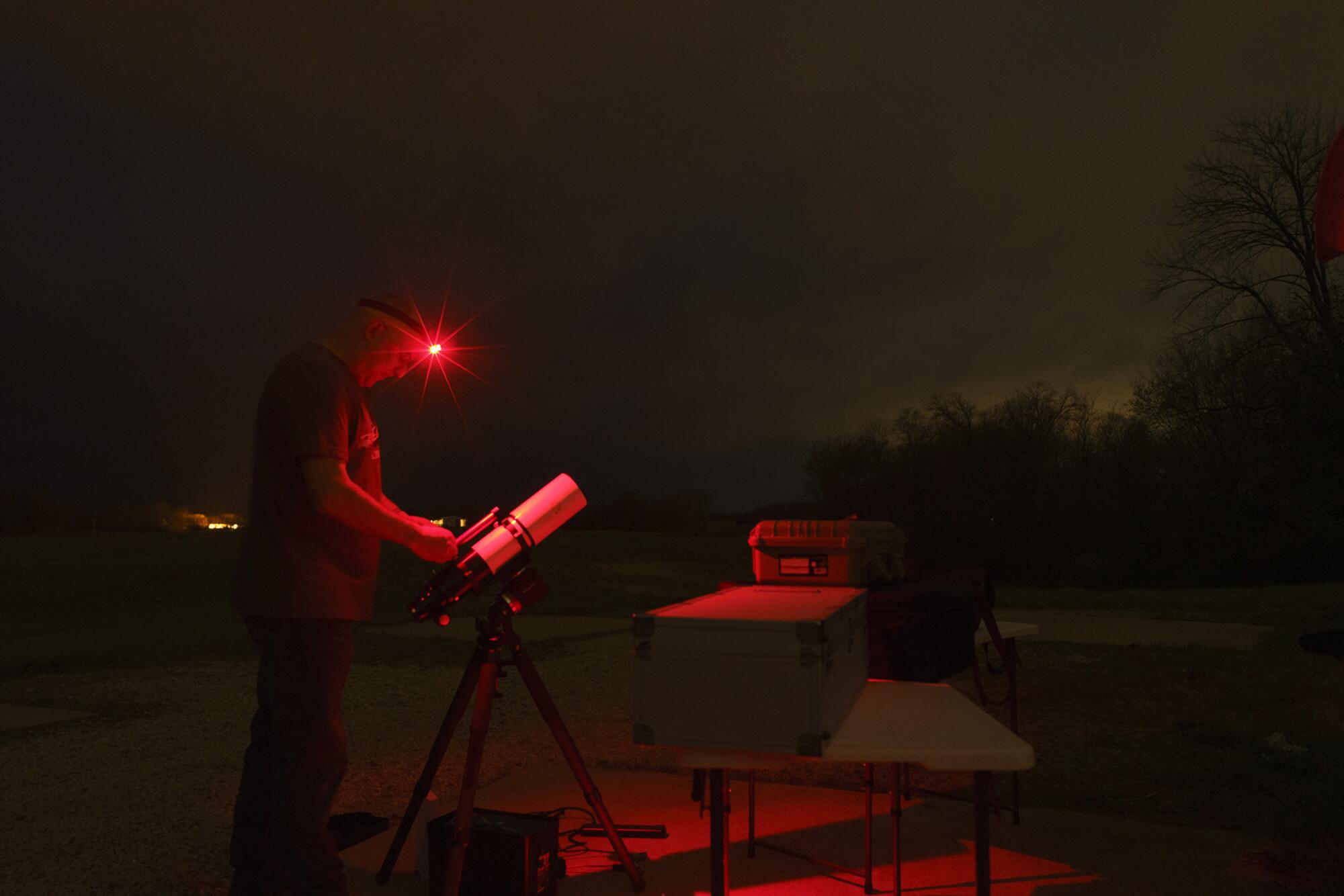 A man wearing a red headlamp with a telescope at night