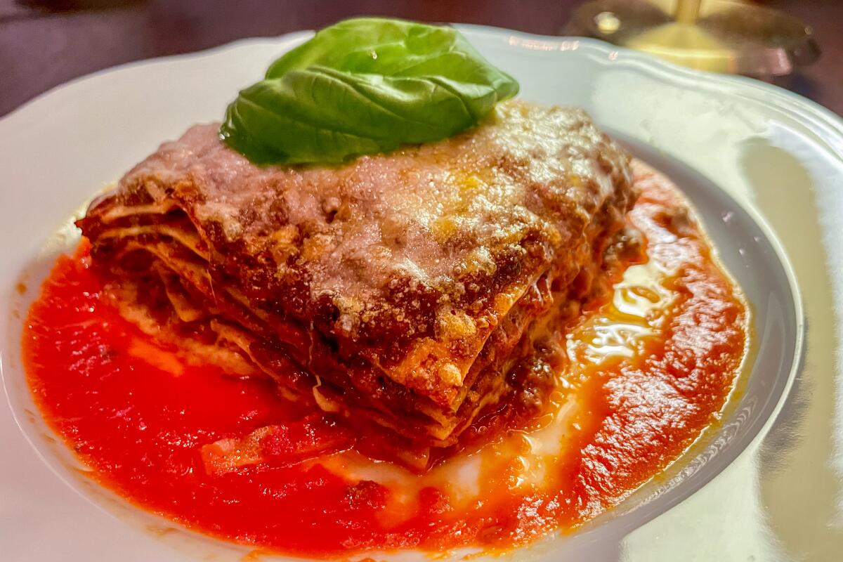 A large square of lasagna topped with a fresh basil leaf