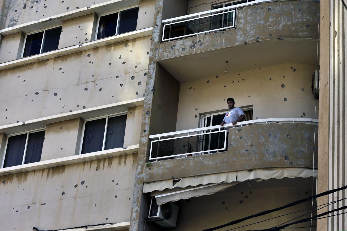 Man standing on balcony of bullet-pocked building