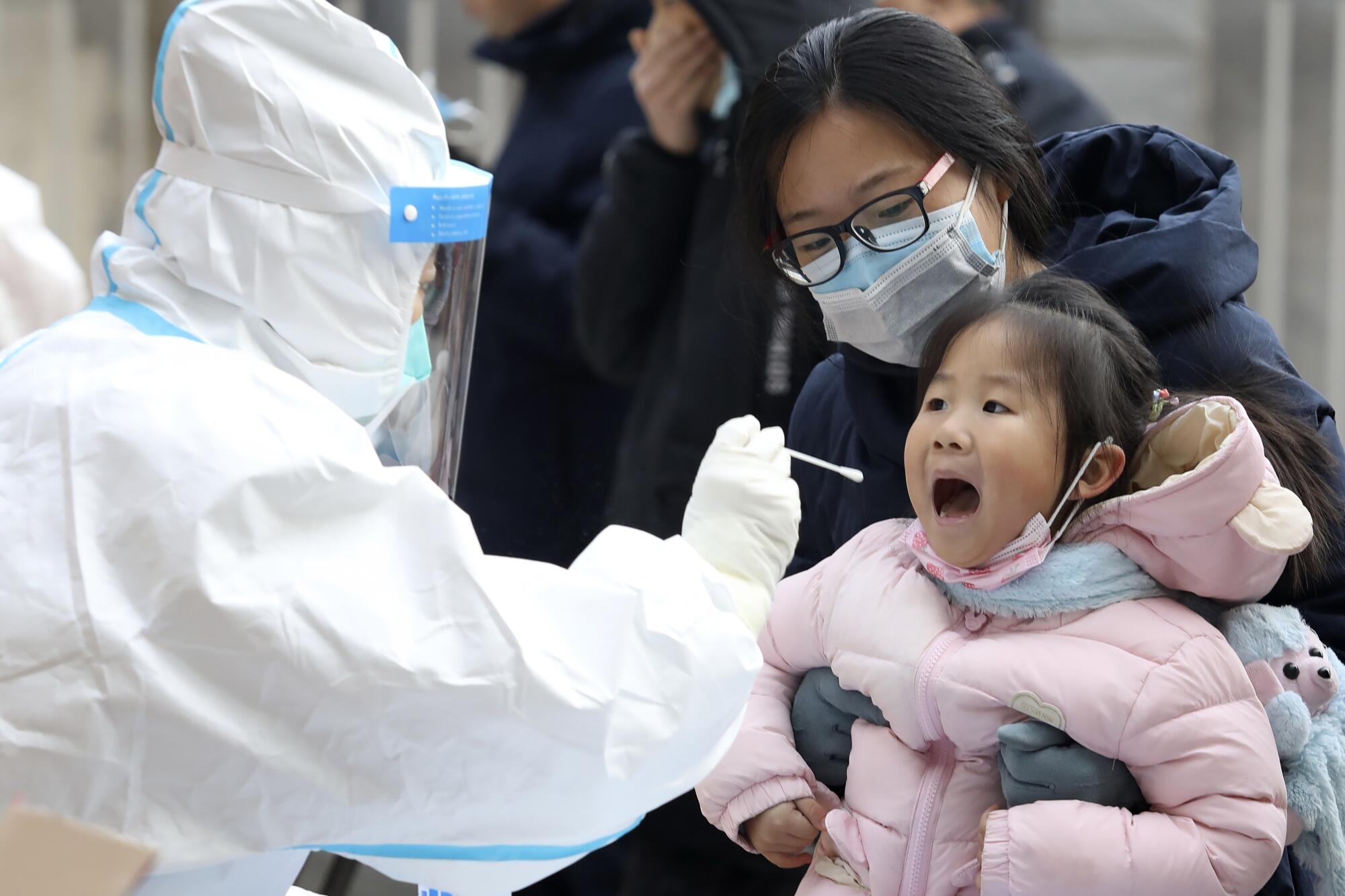 A worker in a protective suit takes a swab from a child for a coronavirus test in Shijiazhuang, in northern China.