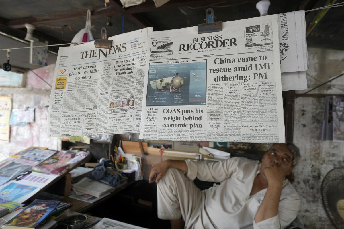 A vendor sits under hanging copies of newspapers.